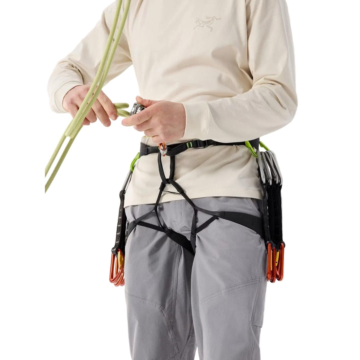 Person wearing arcteryx lithos climbing harness with a beige shirt and gray pants on a light background